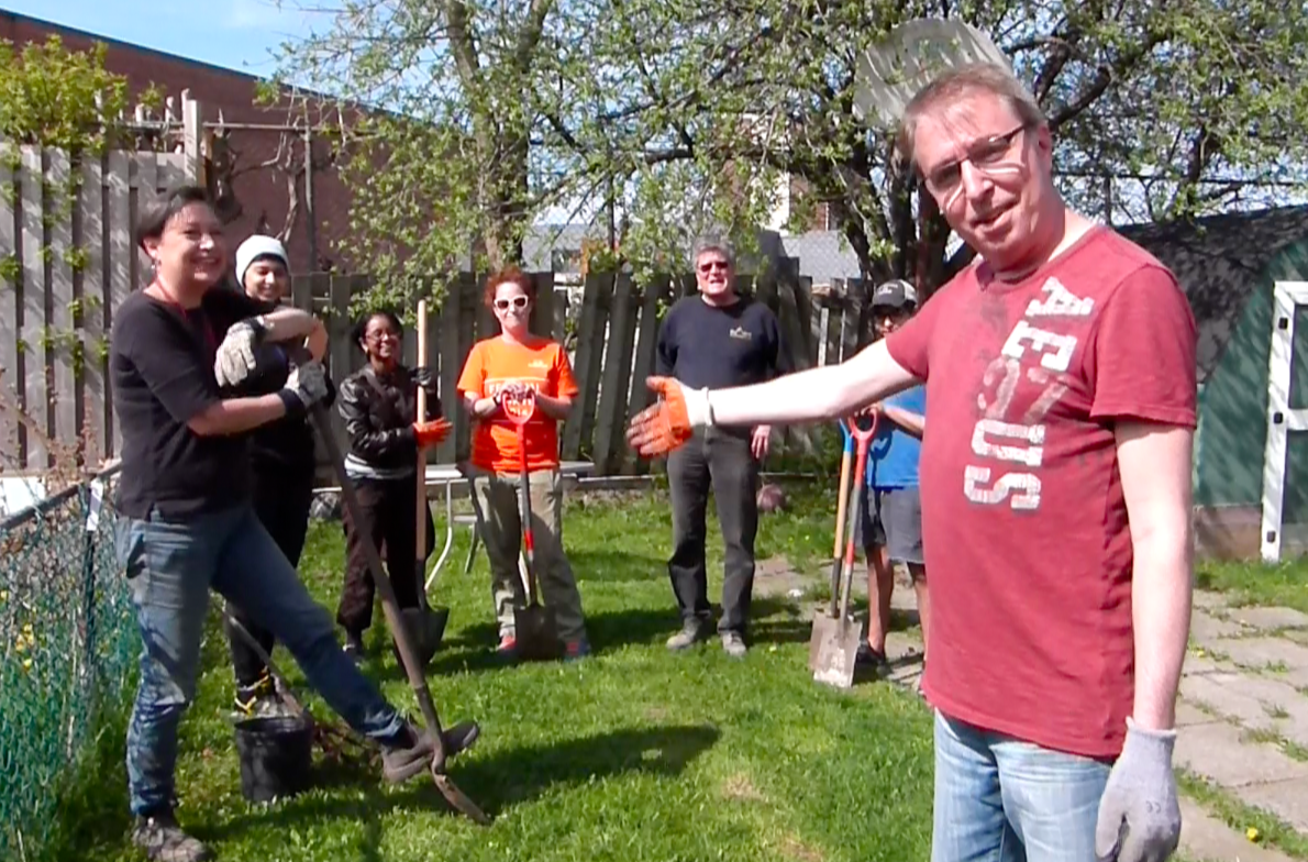 A man wearing gardening gloves points to six volunteers with gardening tools