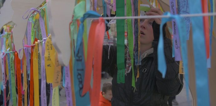A woman hanging a ribbon to join the many others that have messages written on them